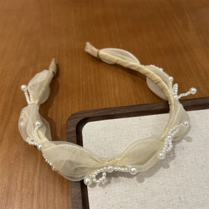 Close-up of beige organza headband with pearls on a wooden surface for luxury hair styling