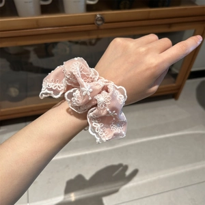 Détail d'un chouchou en dentelle rose avec broderie florale blanche porté au poignet