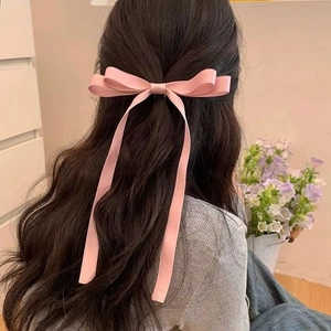 Pink satin bow hair clip with long streamers on female model in cozy interior setting