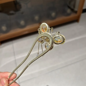 Dettaglio di una forcina dorata a U con farfalla di cristallo colorato e nappa pendente