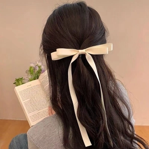 Elegant cream bow hair clip with long ribbons shown on a woman from a back view