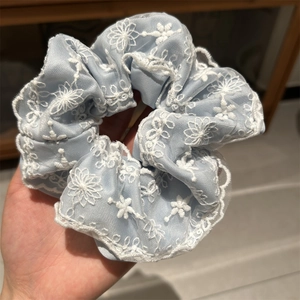 Détail d'un chouchou bleu clair en dentelle avec broderies florales blanches et résille