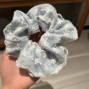 Détail d'un chouchou bleu clair avec broderie florale montrant la texture du tissu fin