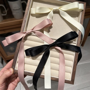 Detail of satin ribbons in cream, pink, and black colors on a wooden jewelry display tray