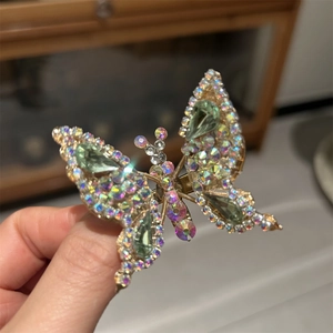 Dettaglio macro di un fermaglio a farfalla con strass cangianti e cristalli verdi a goccia