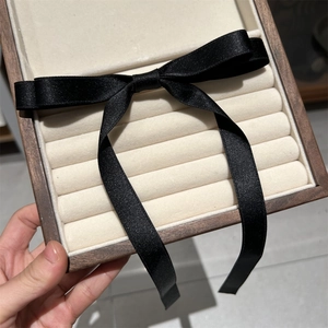 Detail view of walnut wood jewelry box with velvet ring slots and black satin bow