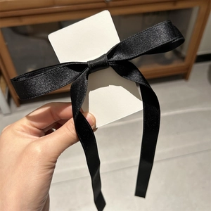 Macro detail of a black satin bow hair clip on card showing glossy silk texture