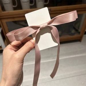 Close-up of pink satin bow hair clip with long ribbons on white display card