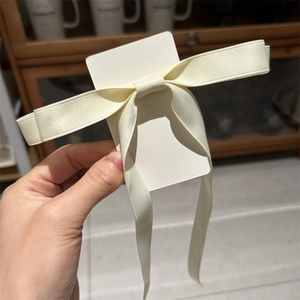Detailed view of a creamy satin ribbon bow hair clip on a white display card