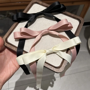 Detailed view of satin bow hair clips in black, soft pink, and beige on a wooden tray