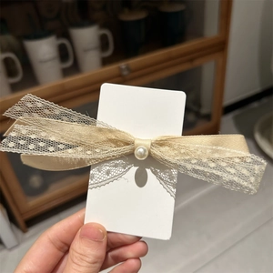Détail d'une pince à cheveux avec nœud en dentelle et perle sur carte de présentation