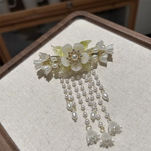 Detail der Vintage-Maiglöckchen-Haarklammer mit weißen Quasten und Perlen auf Stoff
