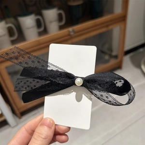Détail d'une pince à cheveux avec nœud en dentelle noire et perle sur carte
