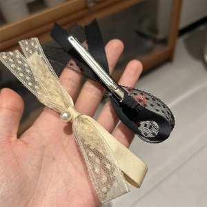 Détail de barrettes nœuds en dentelle beige et noire avec perle et pince crocodile en métal