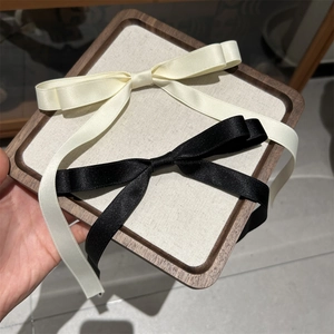 Detailed macro shot of satin bow hair clips in black and off-white on wood background