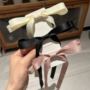 Close-up of three satin bow hair clips in cream, black, and pink on display card