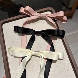 Close-up of three satin bow hair clips in pink, black, and cream with elegant long ribbons