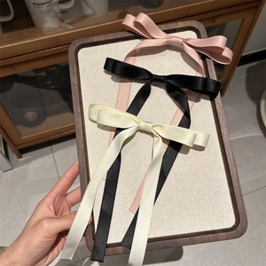 Three satin bow hair clips in pink, black, and cream with long flowing ribbons on a tray
