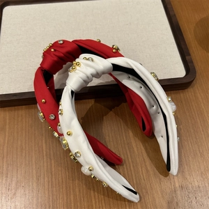 Détail de serre-têtes noués rouge et beige avec ornements en perles et strass brillants