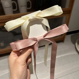 Pair of satin bow hair clips in cream and dusty pink on a card held by hand