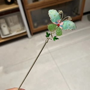 Macro view of gold U-shaped hairpin featuring a green gradient butterfly with floral beads