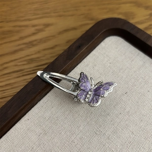 Makroansicht einer lila Emaille-Schmetterlingsspange mit Strass auf einem beigen Tablett