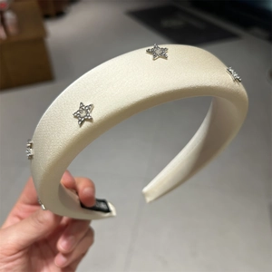 Dettaglio di un cerchietto in raso crema con strass scintillanti a forma di stella