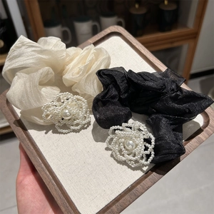 Close-up of elegant black and beige scrunchies featuring woven pearl flower decorations
