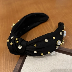 Détail du bandeau en tissu noir avec des perles dorées et des strass transparents décorés