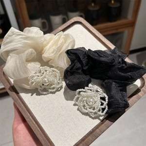 Detailed close-up of pearl camellia hair ties in beige and black organza fabric