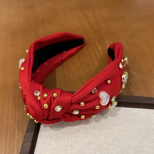 Détail d'un serre-tête noué rouge orné de strass brillants et de perles dorées sur tissu