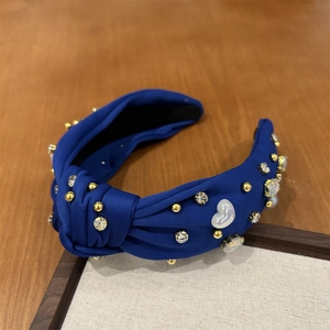 Détail d'un serre-tête noué bleu roi avec perle cœur, strass et clous dorés