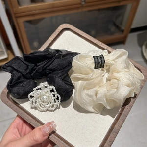 Detailed view of handmade camellia hair ties with pearls on champagne and black organza