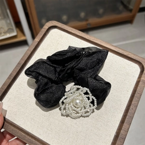 Detailed close-up of a black scrunchie with a woven pearl camellia flower on a wooden tray