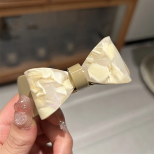 Detailed close-up of marble pattern acetic acid bow hair clip held by hand