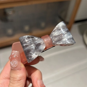 Elegant bow-shaped acetate hair clip with marble grey pattern and peach resin center