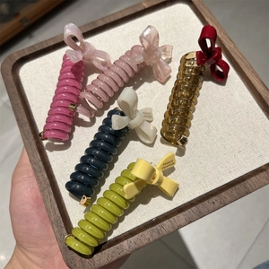 Detailed view of five colorful spiral hair ties with elegant bows on a wooden tray