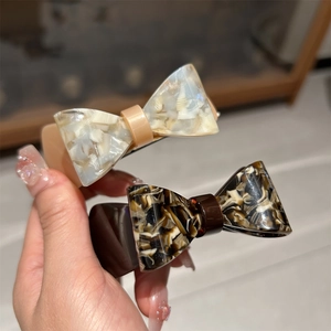 Detail view of two acetate bow hair clips with marble patterns in white and caramel colors