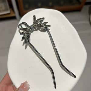 Detail of silver U-shaped hair fork with rhinestone bow and grey crystals on white tray