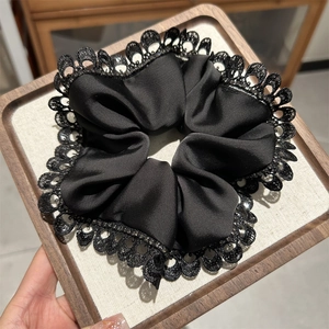Detail of elegant black satin hair scrunchie featuring delicate lace edges and ruffles