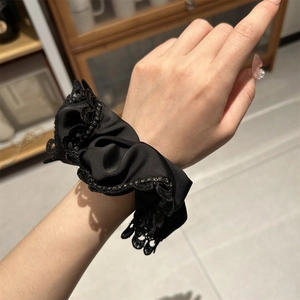 Detail of elegant black lace scrunchie with rhinestones on a wrist in warm lighting