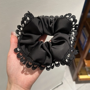 Detailed view of black satin scrunchie with lace edges held in hand for size