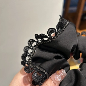 Close-up of black satin hair scrunchie with lace edge and sparkling rhinestone details