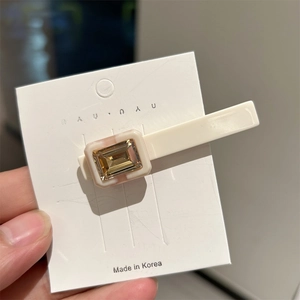 Detail of an ivory acetate hair clip with champagne gold rectangular crystal on card