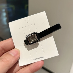 Detail of a black acetate hairpin with a rectangular grey rhinestone on a white display card