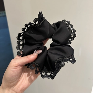 Close-up of black lace scrunchie with rhinestones on textured fabric shown in hand