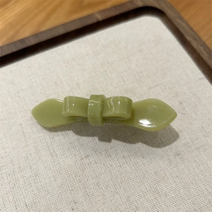 Detail of a minimalist avocado green acetate bow hair clip on a natural wooden tray