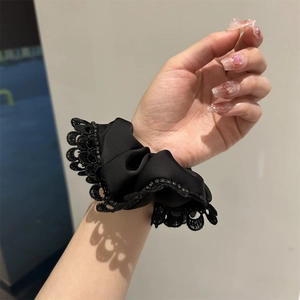 Close-up of black lace scrunchie with satin texture and delicate rhinestones