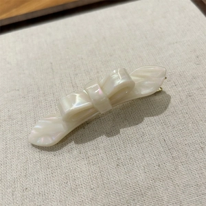 Macro detail of pearl white acetate double-layered bow hair clip with gold metal base