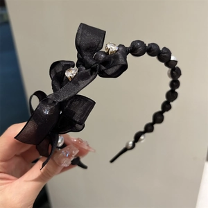Close-up of black silk headband with sparkling rhinestones and elegant faux pearl accents